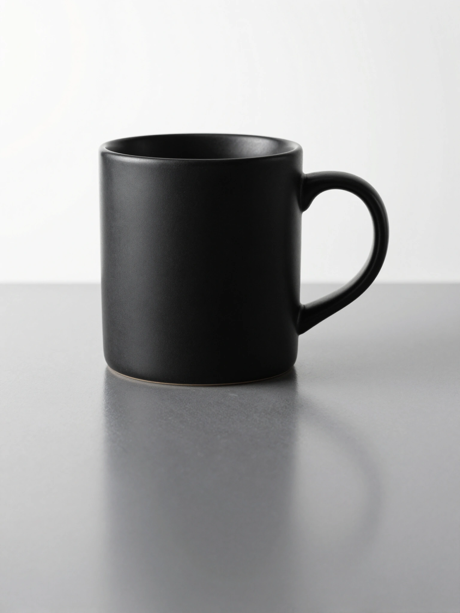 Matte black ceramic mug with cylindrical body and rounded handle on a white background with reflection